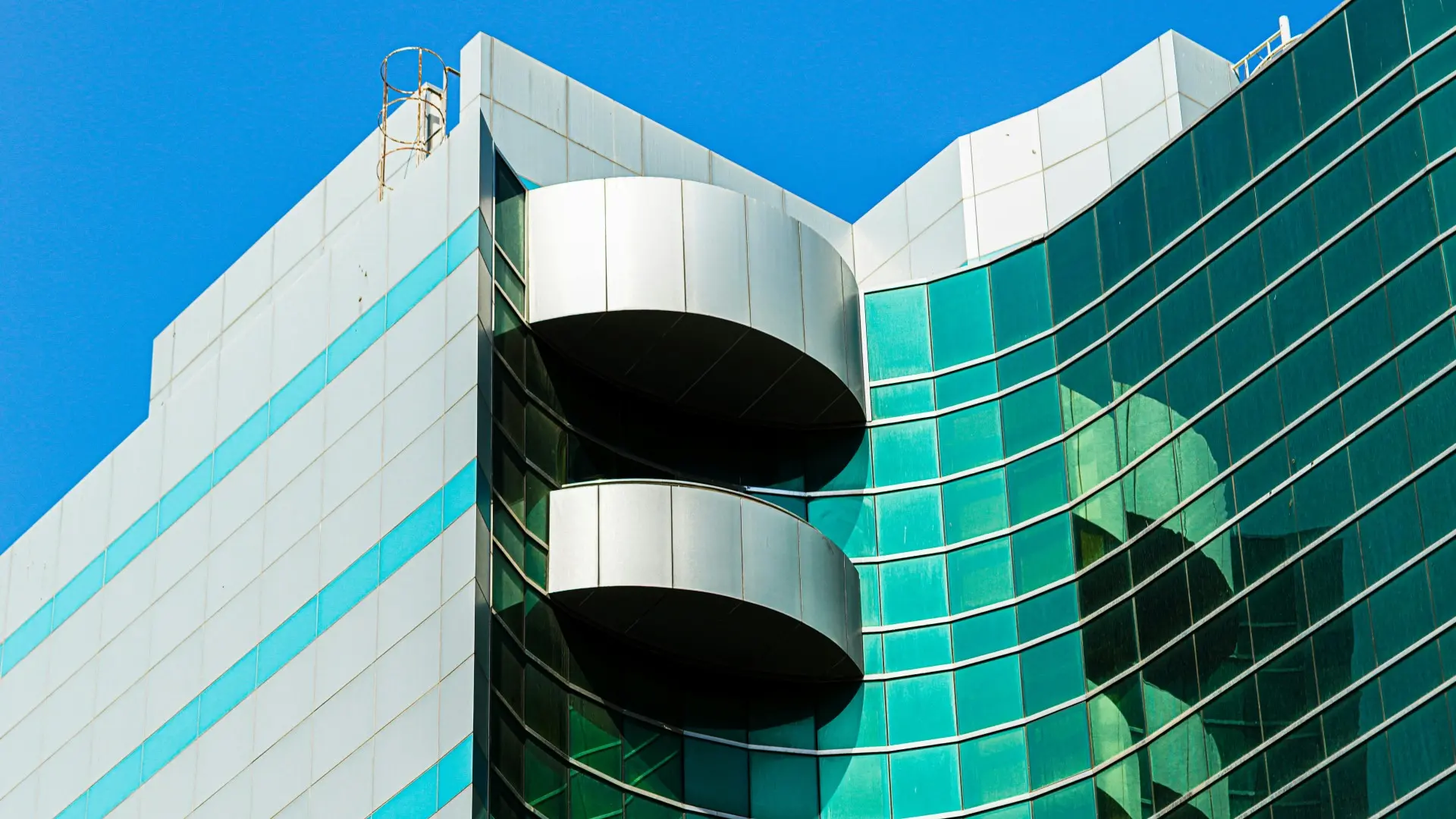 Modern curved glass building with balconies and green-tinted windows